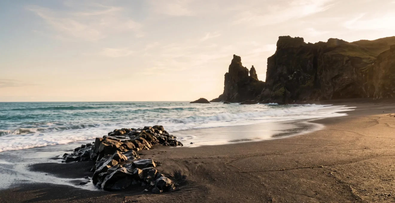 Wide magazine-style photograph of a dramatic black sand beach with ancient volcanic cliffs